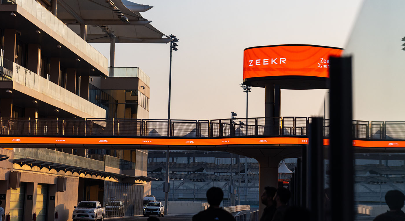 An illuminated orange Zeekr digital promotional billboard sign towering above a pedestrian skybridge path.